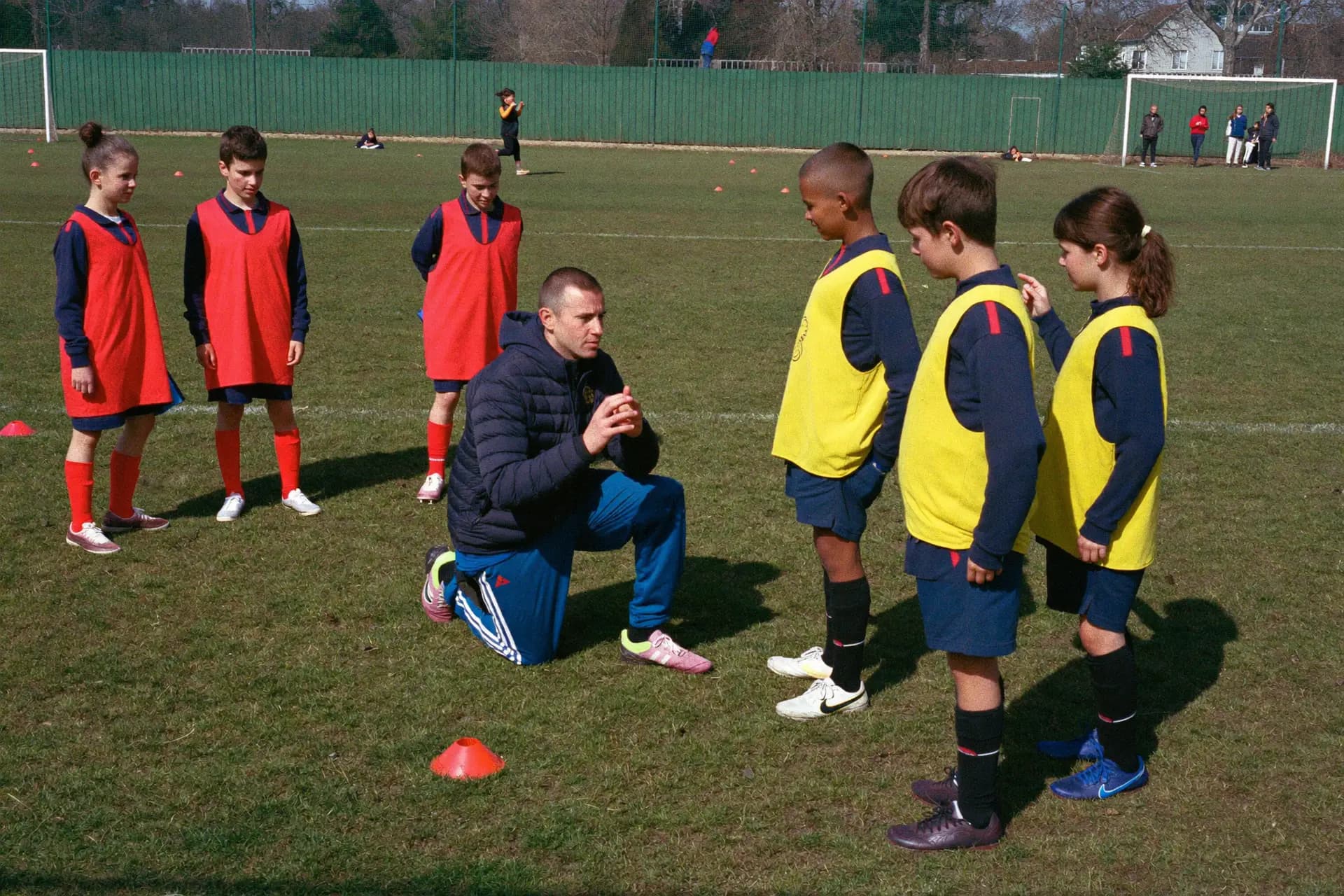 Un éducateur à genoux parle à des enfants en chasubles pendant l'entraînement